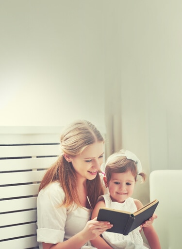 mother reading a book to her daughter on a bench