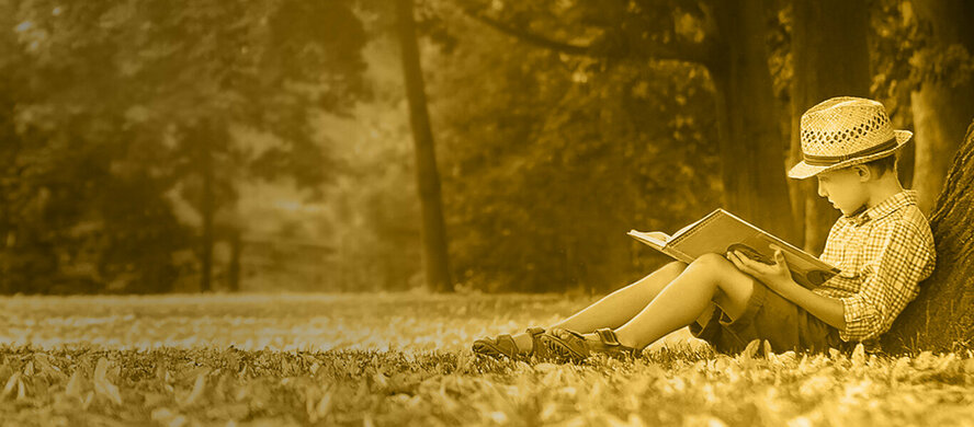 a boy next to a tree reading a book 