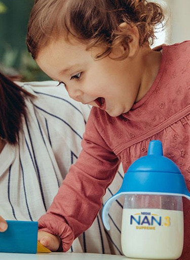 baby girl playing and a bottle of nan milk next to her