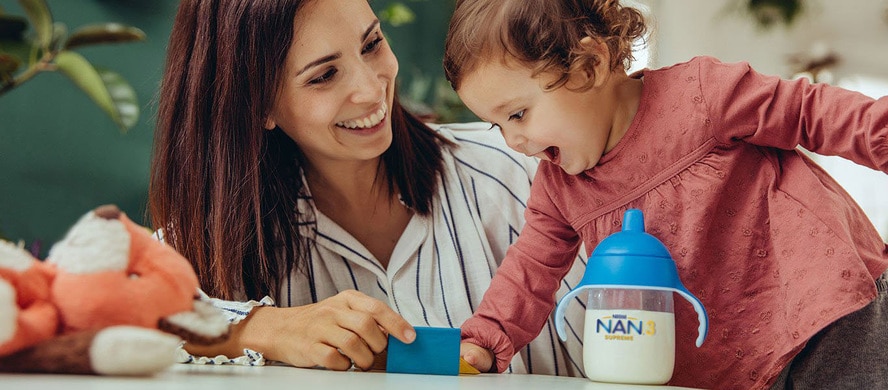 mother and baby girl playing and a bottle of nan milk next to them